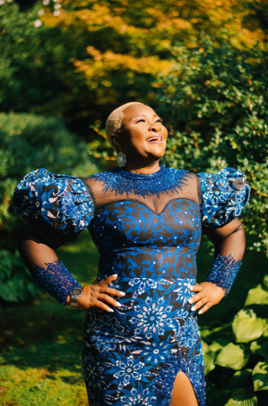 7crop A woman is smiling and looking towards the sun. She's wearing a blue dress that's sparkly.