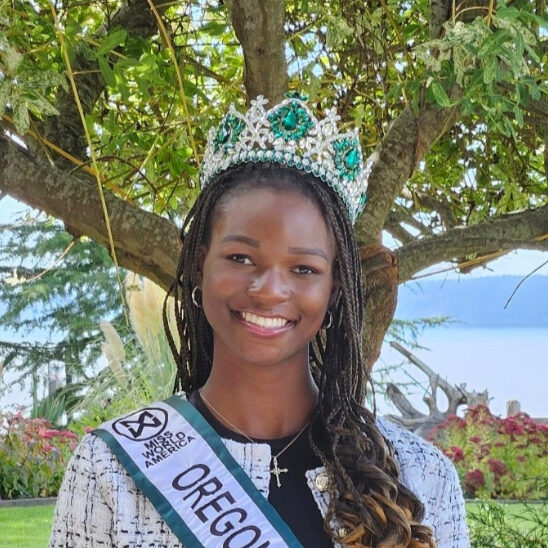 1crop Person wearing a crown and "Oregon" sash, standing outdoors in front of a tree, smiling.