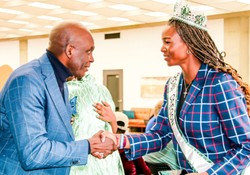 A young woman with long braids is shaking the hands of an older gentlemen. The woman is wearing a crown
