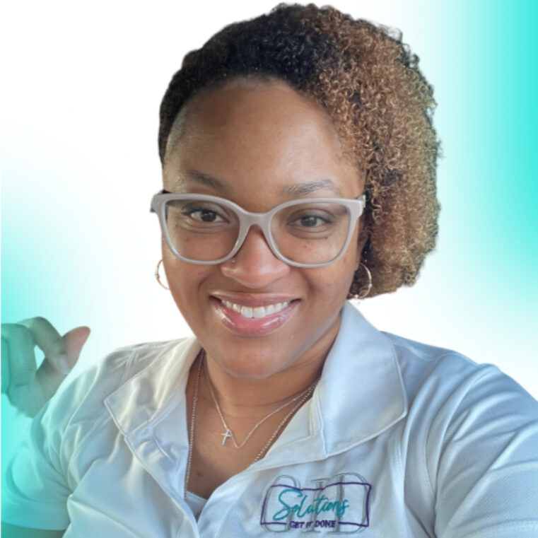 reginacropped2 This is a headshot/ selfie style photo of a woman smiling warmly. She has chin length curly black hair with golden highlights that is styled off to one side. She wears a white collared shirt, a pair of whiteish/gray glasses, small hoop earrings and a tiny cross necklace.